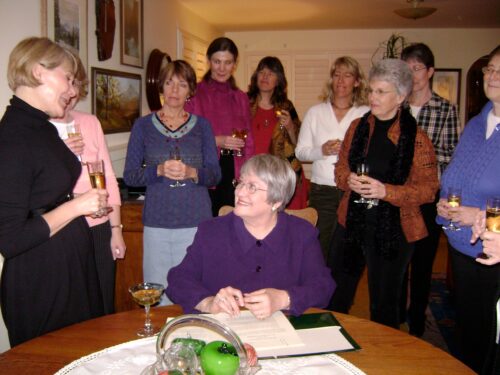 A group of women surround another woman who is sitting at a table with some papers