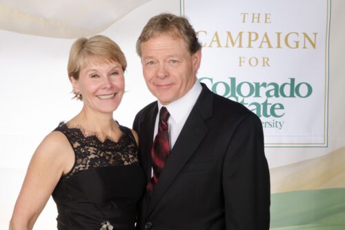 Jodie Hanzlik and her spouse dressued up in a black dress and suit with a Campaign for Colorado State University sign behind them