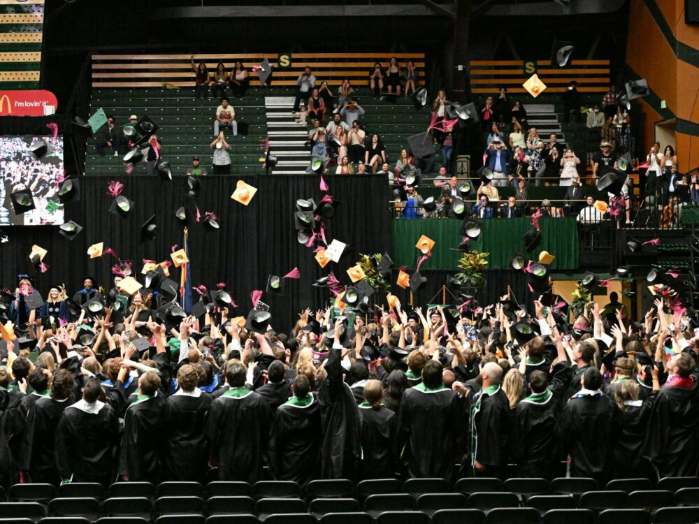 A group of graduating seniors from the College of Health and Human Sciences throw their caps into the air at the commencement ceremony.