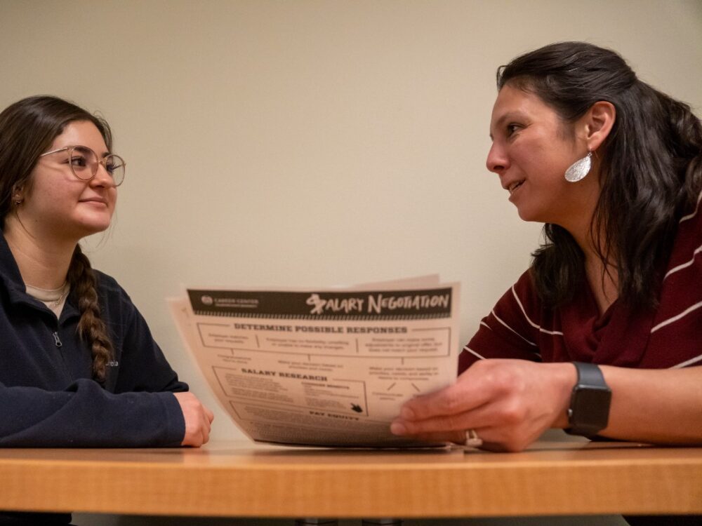 A student sits at a table with a career counselor looking at papers