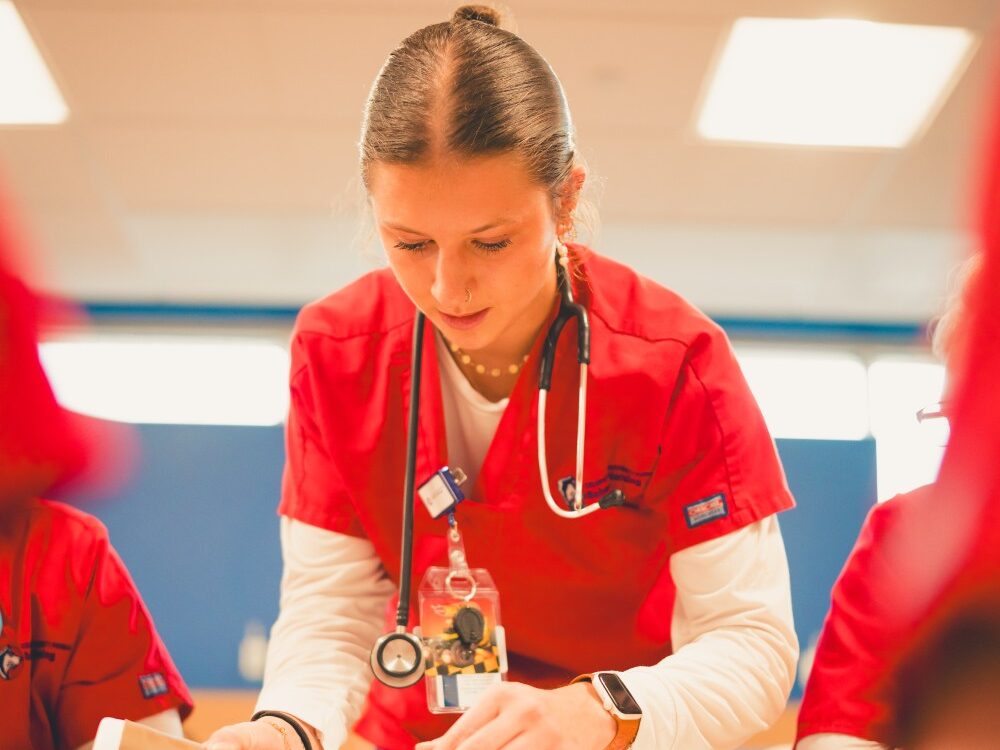 A female nursing student in red scrubs practices IV insertion in a mannequin
