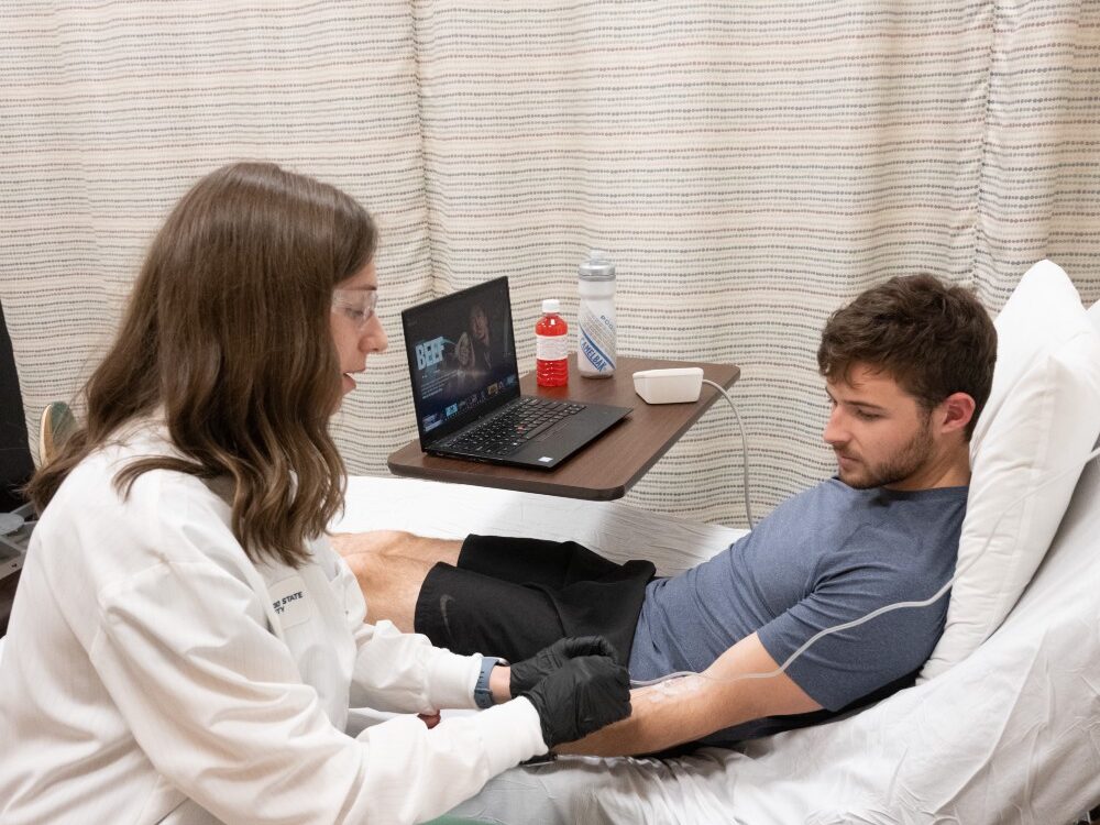 A woman in a white lab coat collects blood samples from a man in a hospital bed