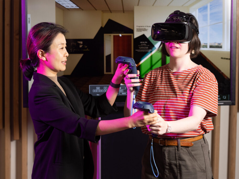 Asian woman guides a college student using virtual reality goggles and wands