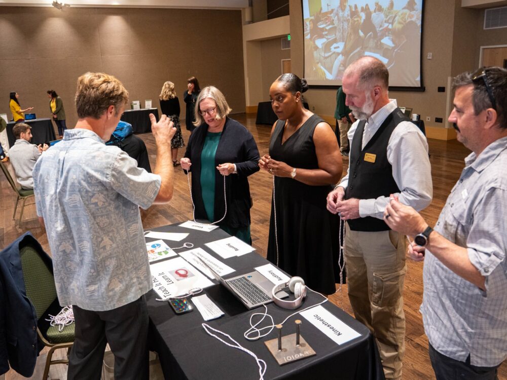 Five university faculty stand around a table in a ballroom discussing creative teaching strategies.
