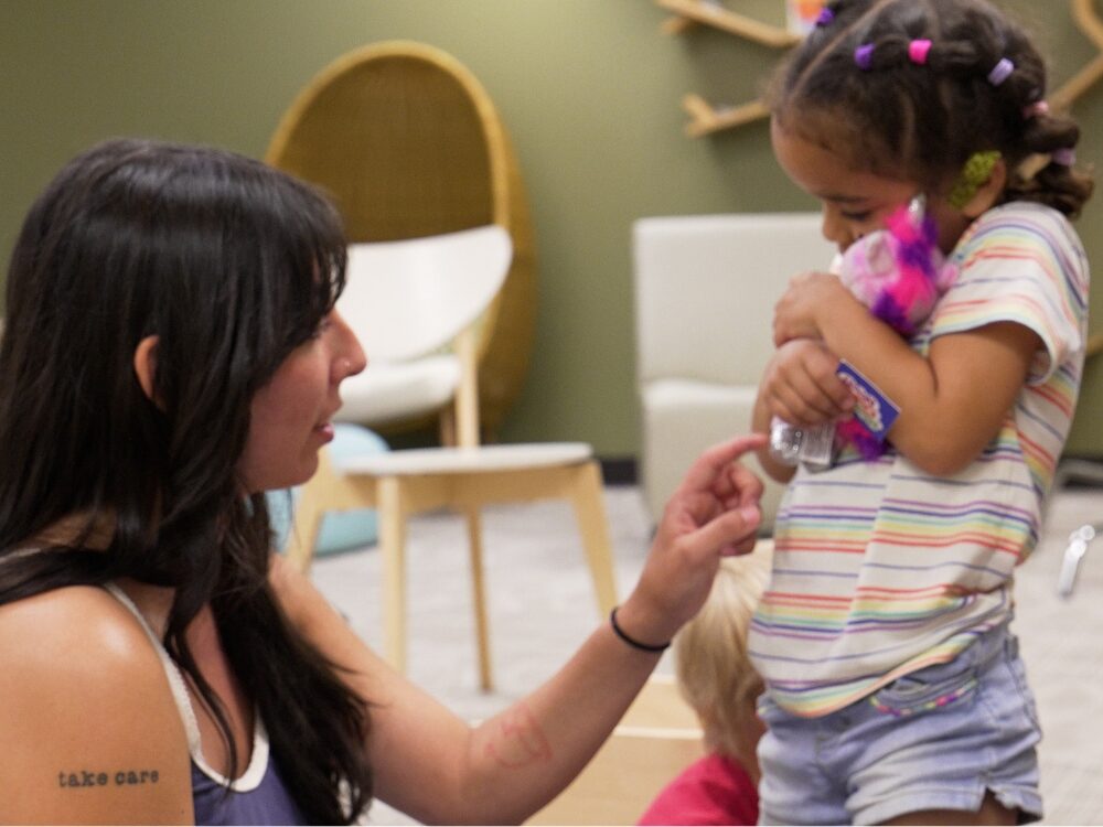 A CSU student smiles while helping a young girl in a classroom