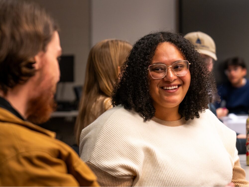 Students smile in a classroom while engaging in a discussion.